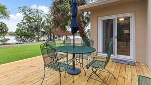 A patio with a round table and chairs, a blue umbrella, and a view of a lake and trees.