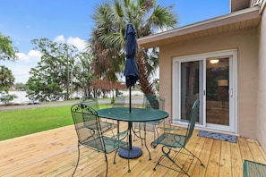 A patio with a round table and chairs, a blue umbrella, and a view of a lake and trees.