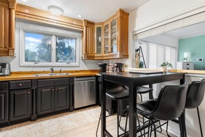A modern kitchen with dark cabinets, a wooden countertop, a double sink, and a bar area with stools. - "Chalet" lake house/walking path/fenced yard/dock (Winter Haven)