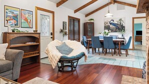 A spacious living area with a dining table, chairs, a cushioned chair, wooden beams, and artwork on the walls. - "Chalet" lake house/walking path/fenced yard/dock (Winter Haven)