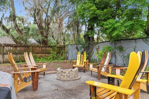A backyard with wooden Adirondack chairs arranged around a stone fire pit.