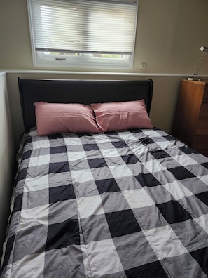 A bed with a checkered bedspread, a black headboard, and a window with blinds.