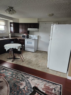 Une cuisine Ă©quipĂ©e dâune cuisiniĂšre, dâun four Ă micro-ondes et dâun rĂ©frigĂ©rateur, une table Ă manger avec des chaises, et un tapis Ă motifs.