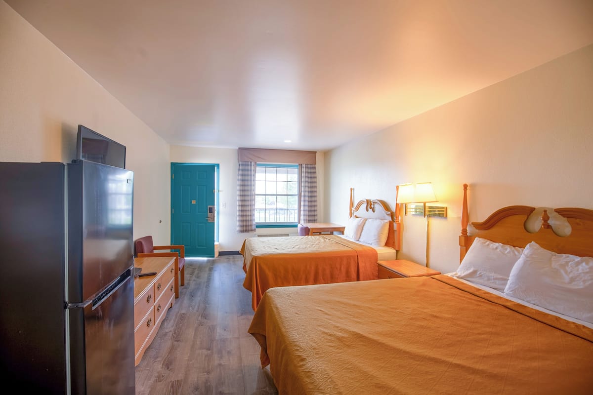Une chambre d’hôtel avec deux lits, un réfrigérateur, une commode en bois, un bureau et une fenêtre avec des rideaux.