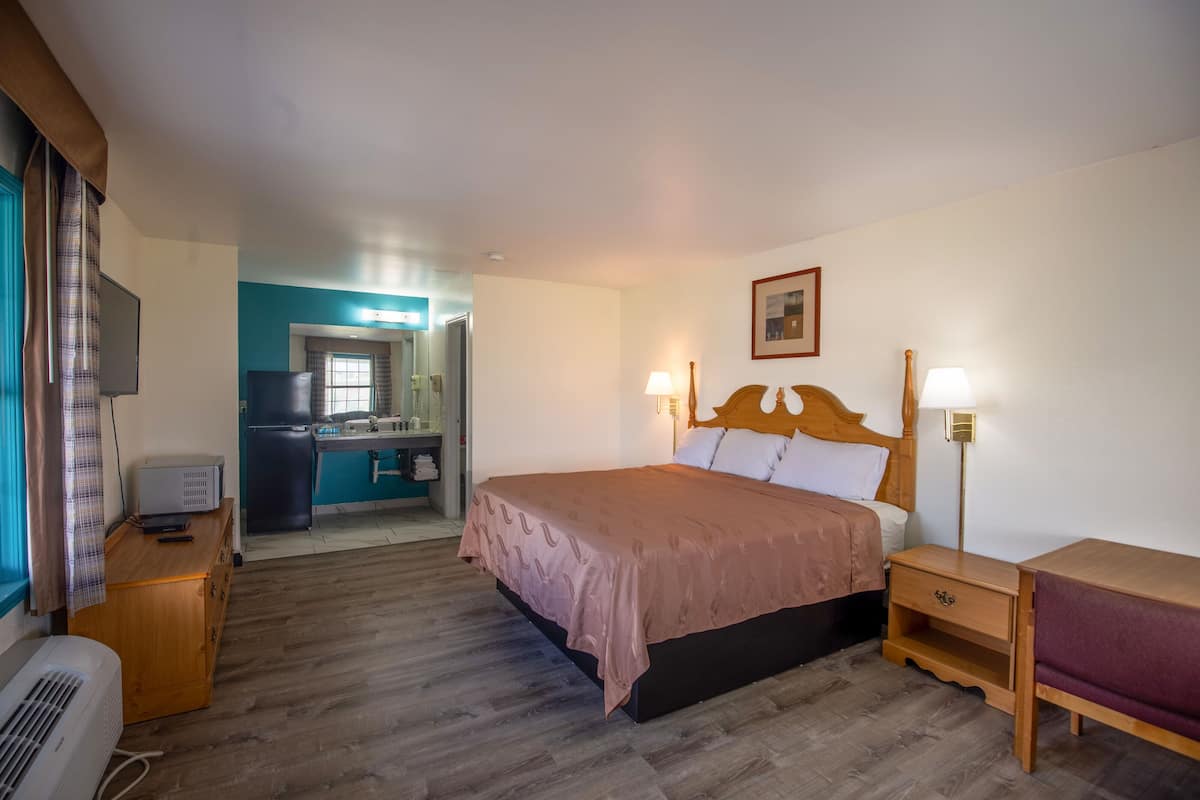 Une chambre d’hôtel comprenant un lit, des lampes de chevet, une table de chevet en bois, un bureau avec un ordinateur et un téléviseur.