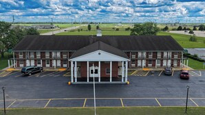 A building with a central entrance, parking lot, and surrounding greenery. - Economy Inn & Suites (Rantoul)