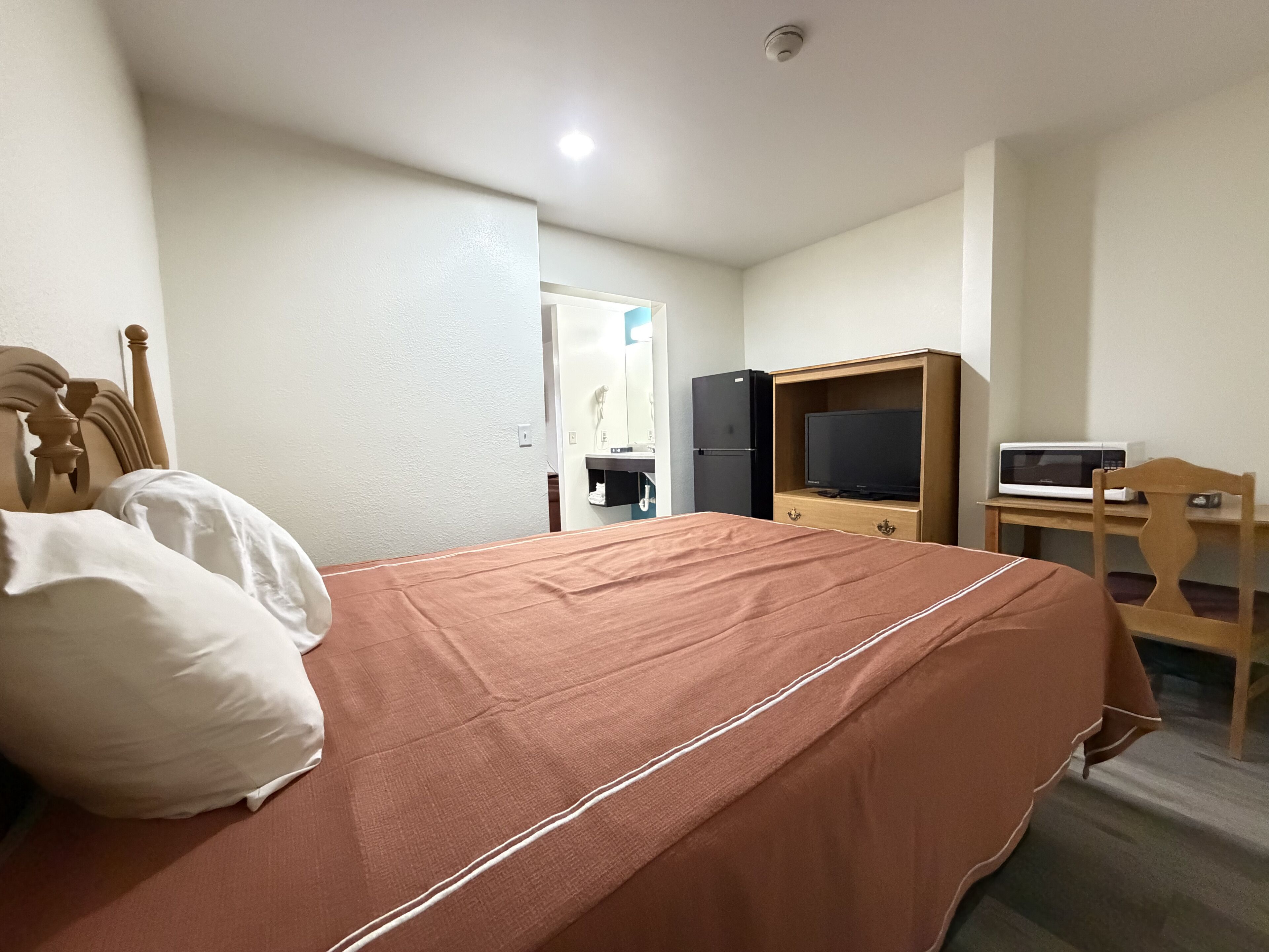 A hotel room with a bed, a television, a microwave, and a wooden desk.