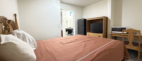 A hotel room with a bed, a television, a microwave, and a wooden desk.