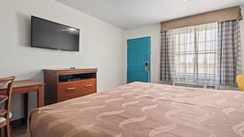 Een hotelkamer met een bed, een bureau, een televisie, een blauwe deur en een raam met gordijnen.