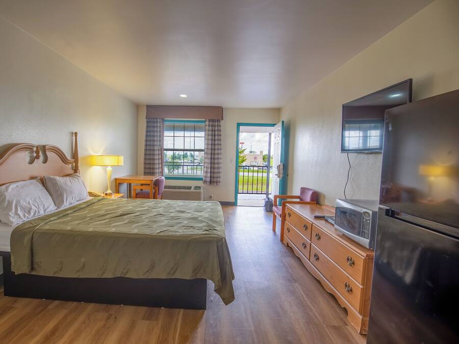A hotel room with a bed, dresser, television, and a view of the outdoors.