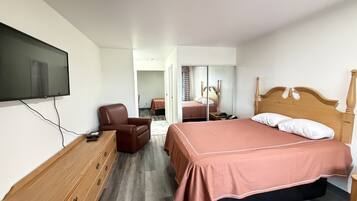 Une chambre d’hôtel avec un lit, une télévision, une commode en bois, une chaise et un miroir.