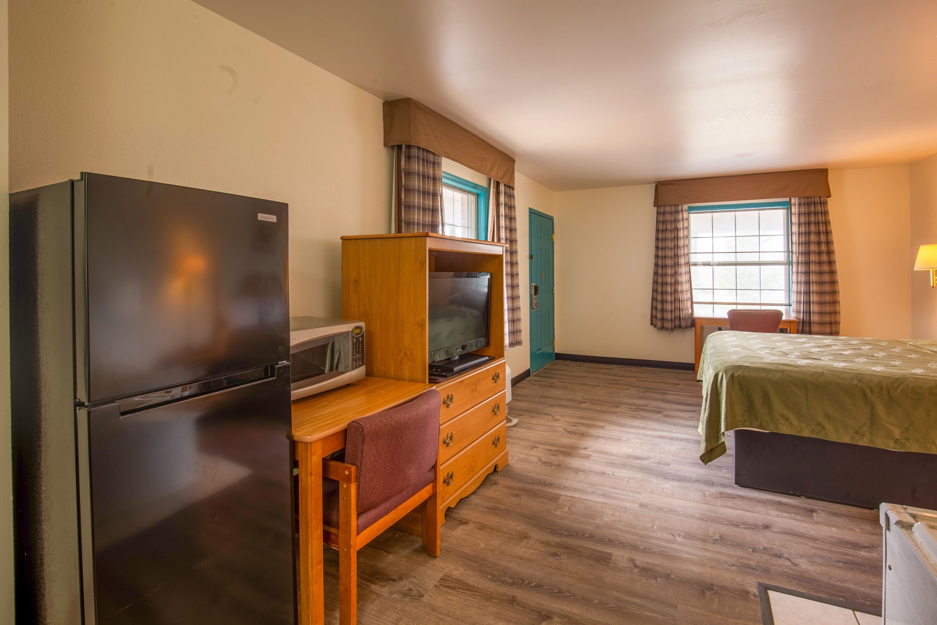 A compact room with a bed, a desk with a chair, a television, a microwave, and a refrigerator.