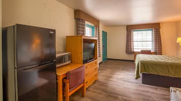 A compact room with a bed, a desk with a chair, a television, a microwave, and a refrigerator.