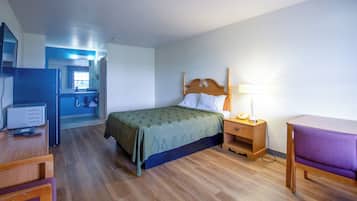 Een kamer met een bed, een bureau, een stoel, een nachtkastje, een lamp en een bijzettafeltje.