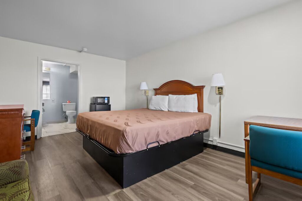 A hotel room with a bed, bedside lamps, a desk, a chair, and a small desk with a computer.