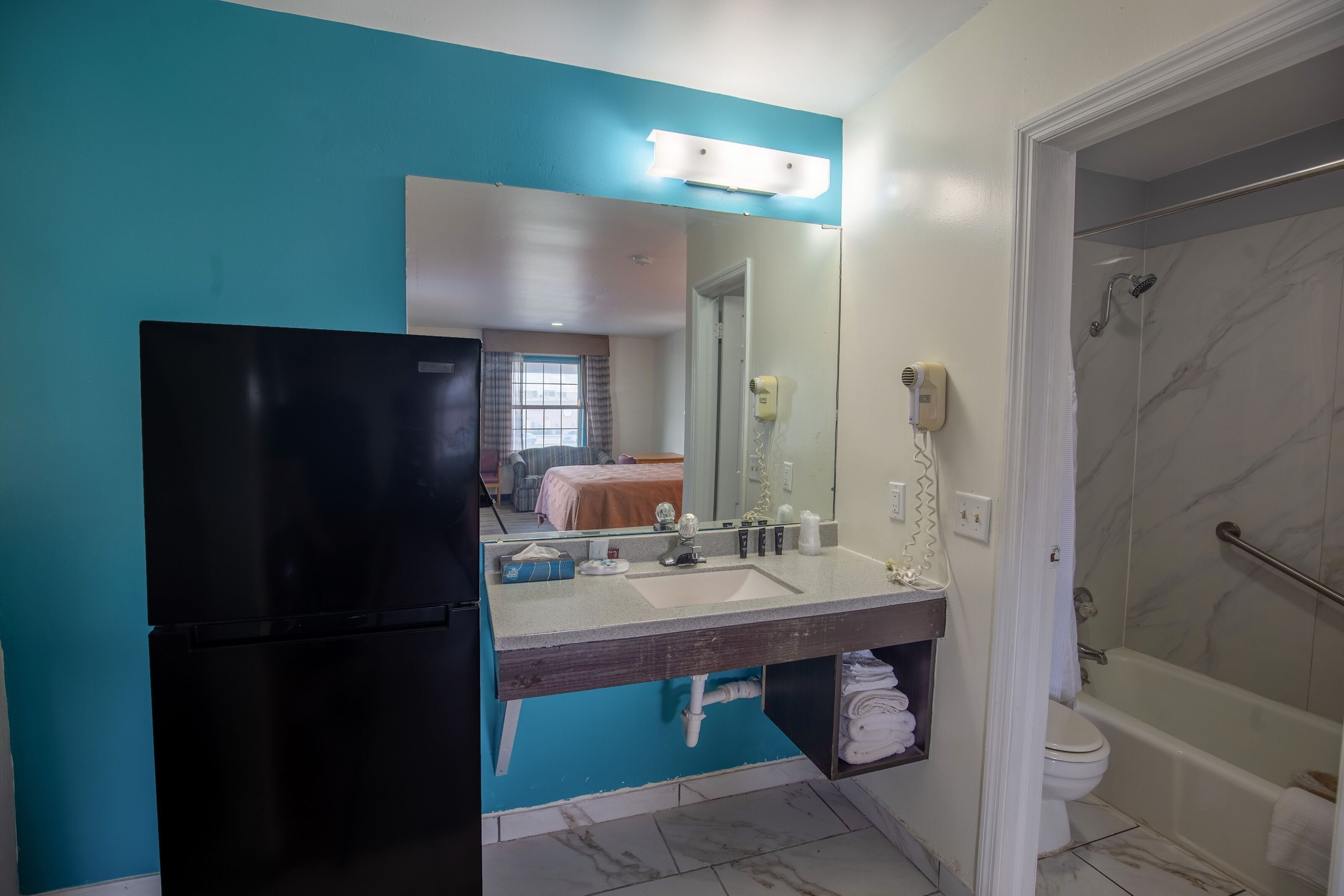 A bathroom with a black refrigerator, a sink with a mirror, a shower, and a toilet.