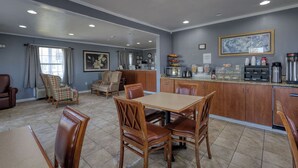 A dining area with a table and chairs, a kitchen area with appliances, and a living area with a couch and chairs. - Economy Inn & Suites (Rantoul)
