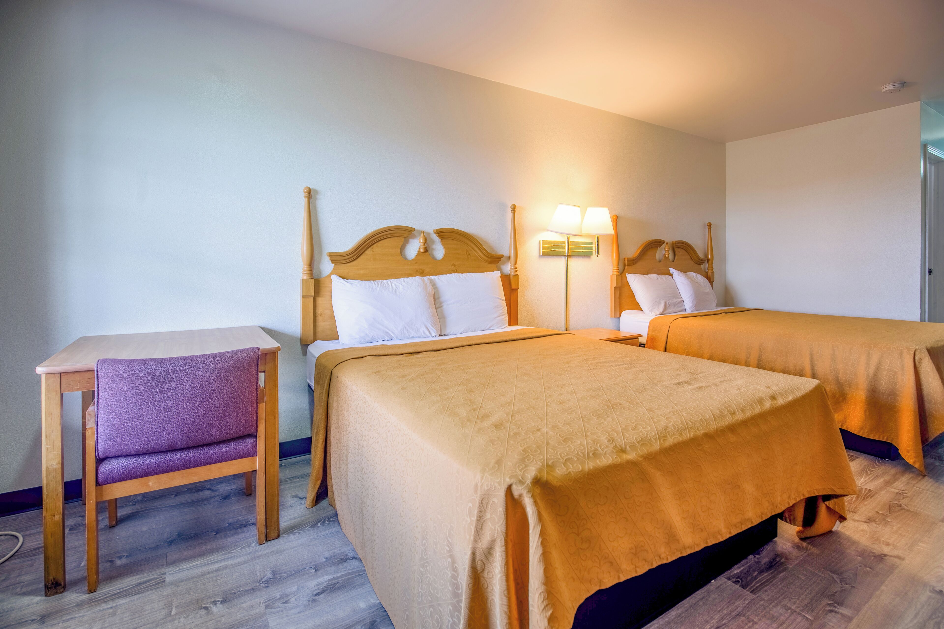 A hotel room with two beds, a small table, and a chair.