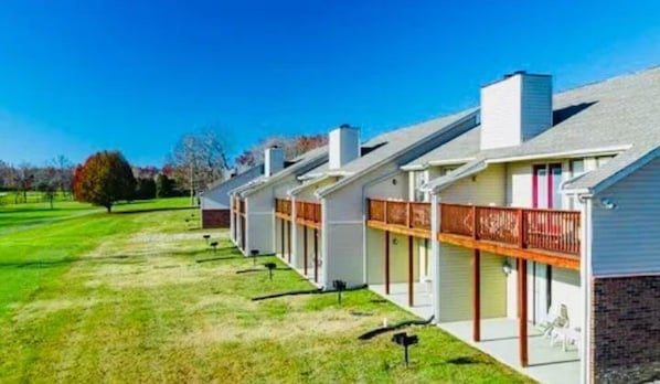 A row of single-story houses with attached porches, a well-maintained lawn, and a clear blue sky.