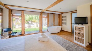 A modern room with a large bathtub, a television, and a view of a garden. - Airy Barn Conversion, Private Parking & Garden (Burrington)