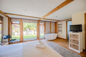 Ein modernes Zimmer mit einer großen Badewanne, einem Fernseher und Blick auf einen Garten.
