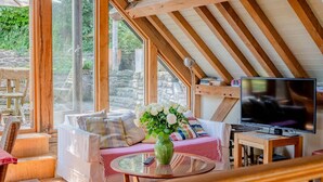 A cozy room with a wooden ceiling, a sofa with cushions, a glass table with a vase, and a television. - Airy Barn Conversion, Private Parking & Garden (Burrington)