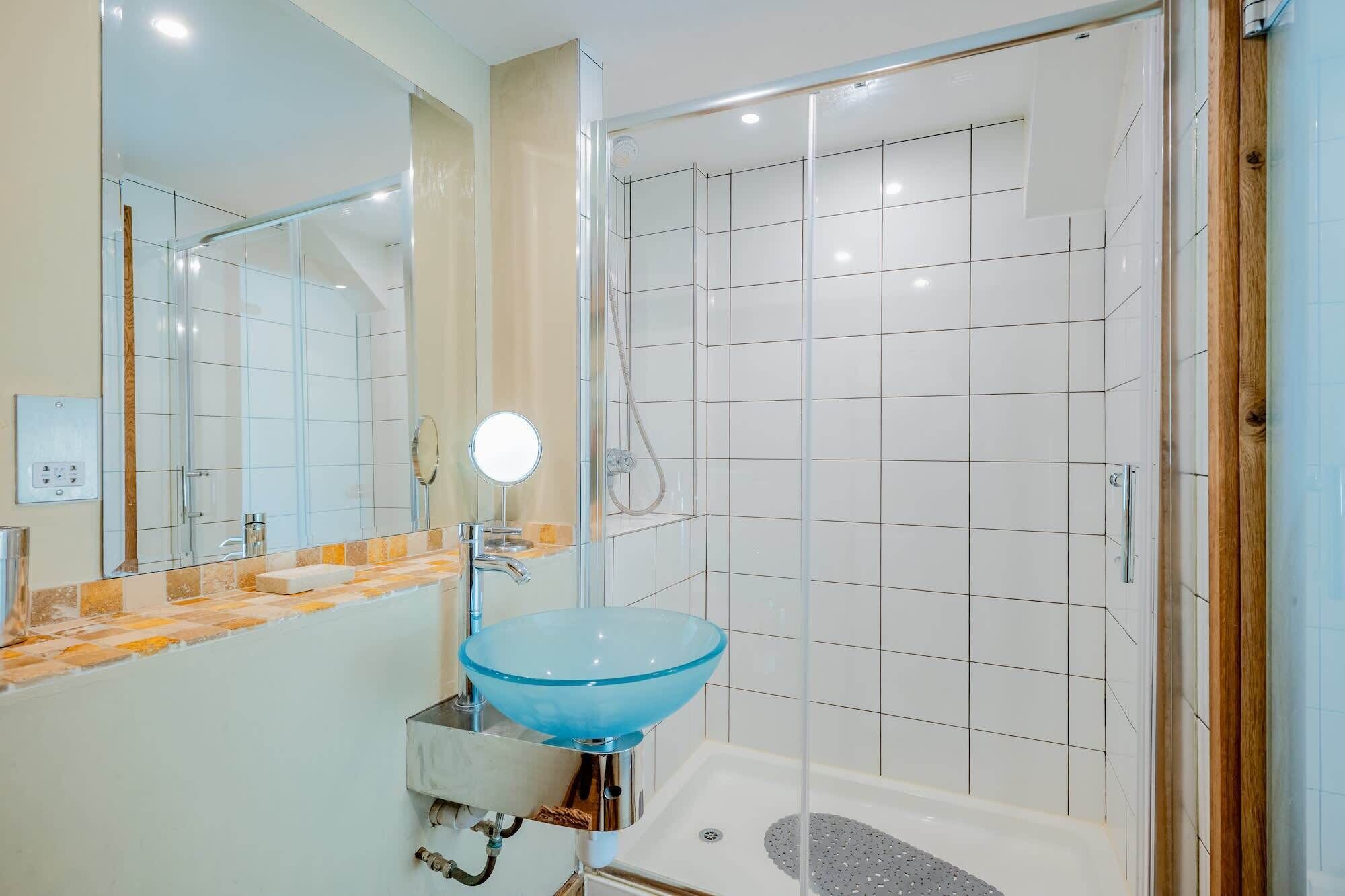 A bathroom with a glass shower enclosure, a blue glass sink, and a mirror.