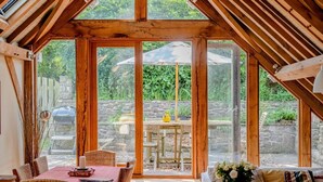 A cozy room with a wooden ceiling, large windows, a dining table, and wicker furniture. - Airy Barn Conversion, Private Parking & Garden (Burrington)