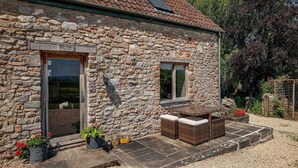 Un edificio de piedra con dos ventanas, una puerta y un pequeño espacio al aire libre con mesa y sillas.