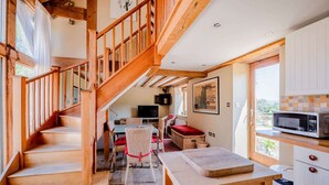 Una escalera de madera lleva a un comedor con mesa y sillas, una cocina con microondas, y un ventanal con vistas.