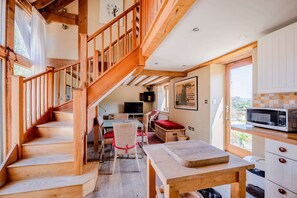 Eine Holztreppe führt zu einem Essbereich mit Tisch und Stühlen, einer Küche mit Mikrowelle sowie einem Fenster mit Blick.