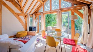 A cozy room with a bed, a TV, a glass table with chairs, and large windows. - Cosy Studio with Patio, Seating & Private Parking (Burrington)