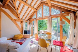 A cozy room with a bed, a TV, a glass table with chairs, and large windows. - Cosy Studio with Patio, Seating & Private Parking (Burrington)