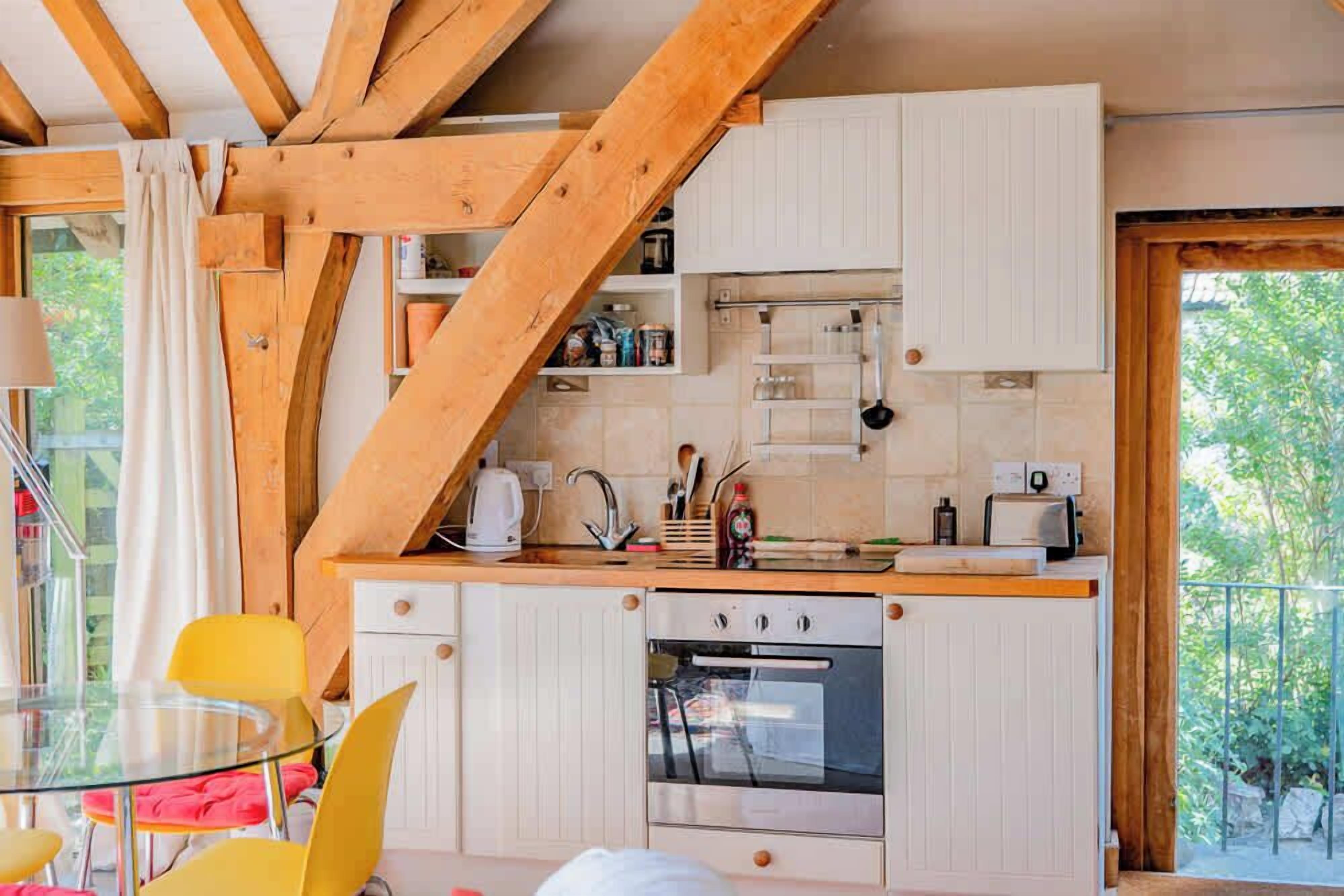 A kitchen with wooden beams, white cabinets, a glass table, and yellow chairs.