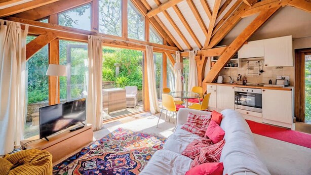 A cozy interior with a TV, sofa, dining table, chairs, kitchen, and large windows. - Cosy Studio with Patio, Seating & Private Parking (Burrington)