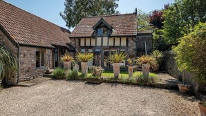 A stone building with a tiled roof, a gravel driveway, and potted plants. - Cosy Studio with Patio, Seating & Private Parking (Burrington)