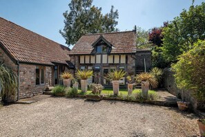 A stone building with a tiled roof, a gravel driveway, and potted plants. - Cosy Studio with Patio, Seating & Private Parking (Burrington)
