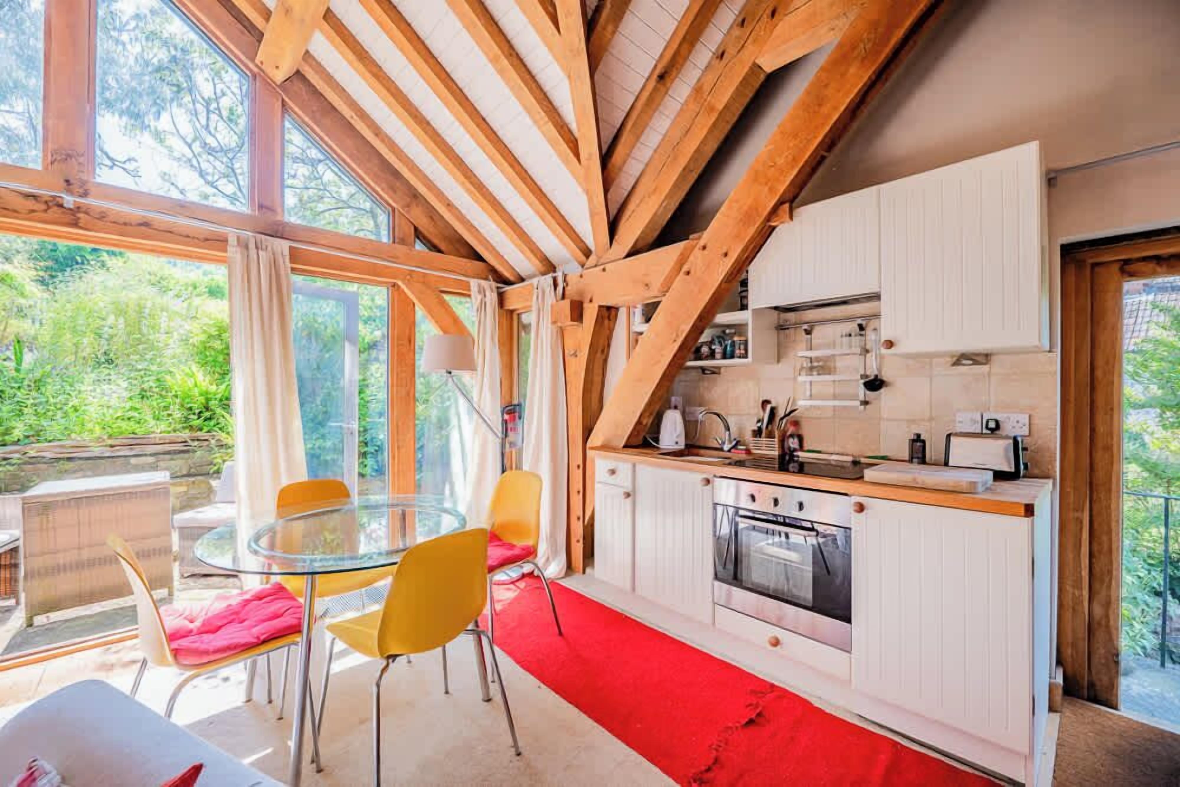 A modern kitchen with wooden beams, a glass table, and yellow chairs.