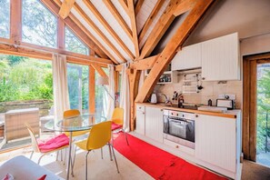 A modern kitchen with wooden beams, a glass table, and yellow chairs. - Cosy Studio with Patio, Seating & Private Parking (Burrington)