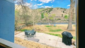 Un patio con mobiliario exterior, una parrilla y vistas a un río y colinas.