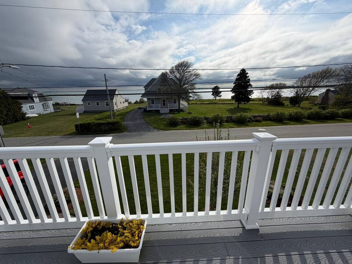 A wooden deck with a white railing, a planter with yellow flowers, and a view of houses and a road in the background.