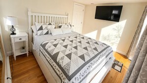 A bedroom with a bed, a nightstand, a TV, and a window with curtains. - Backyard Retreat / 5 Min > Beach & Main St (Fairhaven)