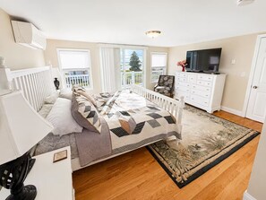 Un dormitorio con cama, cómoda, televisor y vistas al exterior.