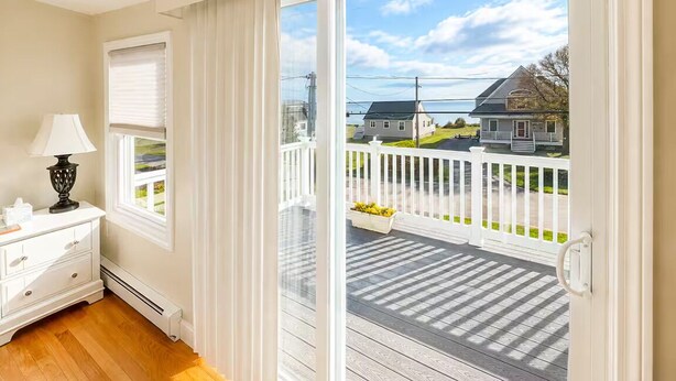 A room with a white dresser, a lamp, a window with blinds, and a view of a deck and houses outside. - Backyard Retreat / 5 Min > Beach & Main St (Fairhaven)