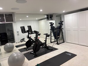 Ein Heimfitnessraum mit Trainingsgeräten, darunter ein Ergometer, ein Crosstrainer und eine Gewichtbank.