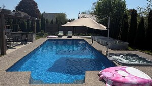 A rectangular swimming pool with a tiled deck, lounge chairs, and a covered seating area. - A vacation home from home (Hamilton)