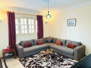 A living room with a grey sectional sofa, red cushions, a small wooden side table, a cowhide rug, and a hanging light fixture.