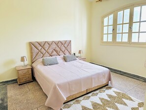 A bedroom with a bed, two bedside tables, a window, and a patterned rug.