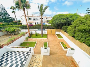 A courtyard with a checkered floor, white walls, and a view of a building in the background.