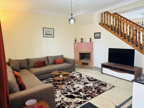 Ett vardagsrum med en soffa, ett soffbord, en öppen spis, en tv och en trappa.